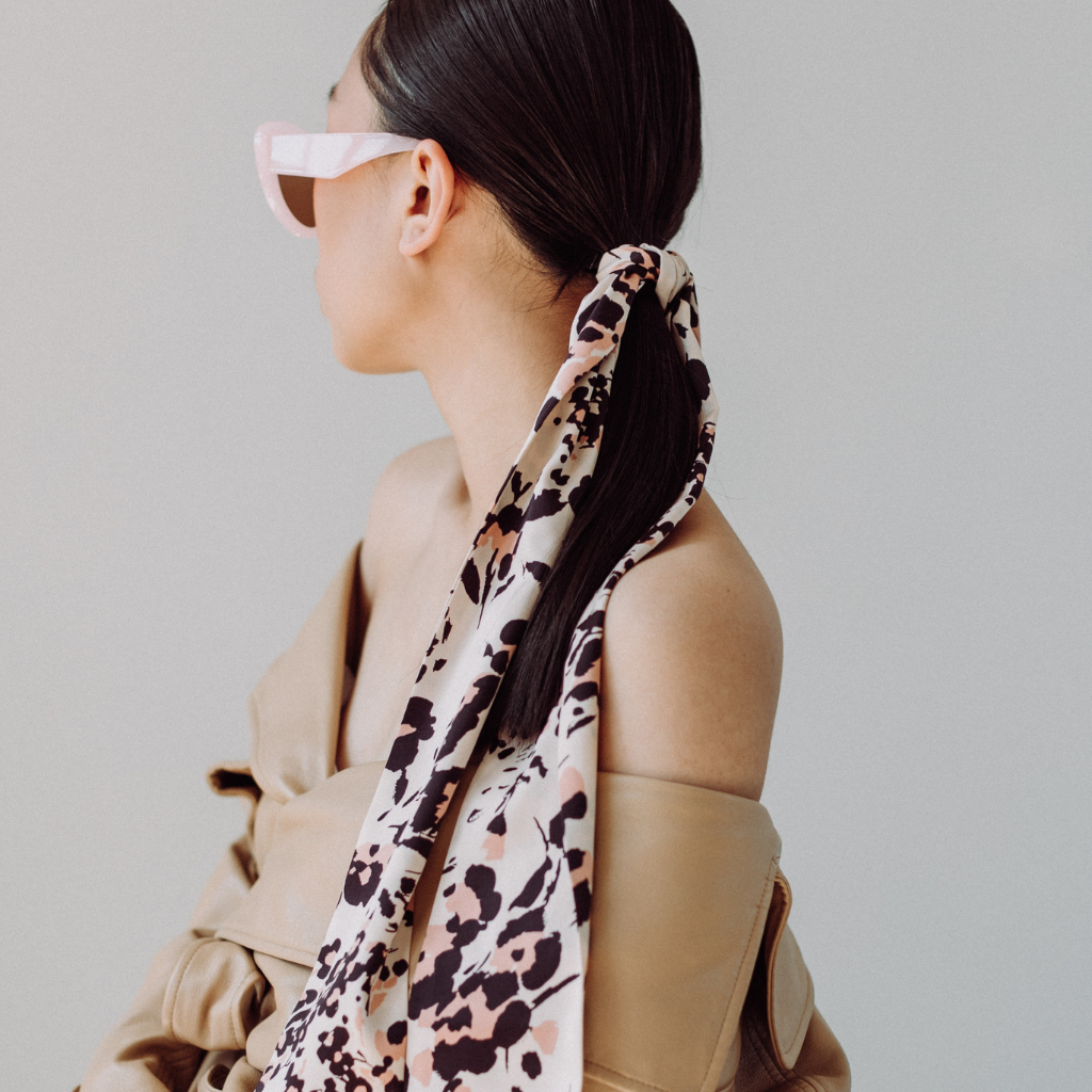 Person wearing a leopard print scarf as a hair tie with a plain background